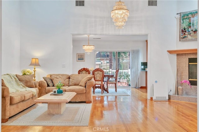 living room featuring a chandelier, wood finished floors, a towering ceiling, and a tiled fireplace