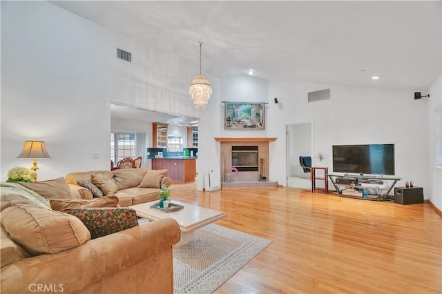 living area featuring high vaulted ceiling, a chandelier, light wood-type flooring, a tile fireplace, and recessed lighting
