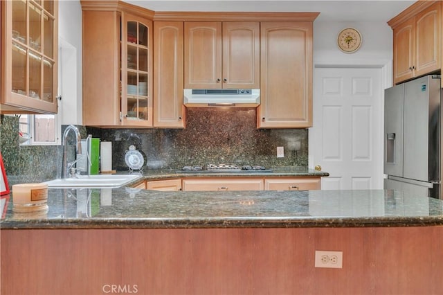 kitchen featuring under cabinet range hood, gas stovetop, dark stone countertops, and stainless steel fridge with ice dispenser