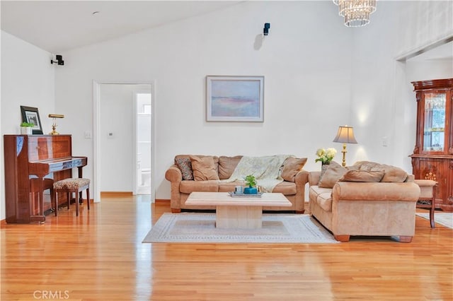 living area featuring light wood-style flooring, a chandelier, high vaulted ceiling, and baseboards