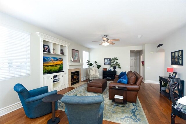 living room featuring wood finished floors, a ceiling fan, a fireplace, and baseboards