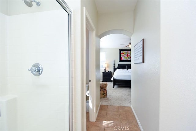 ensuite bathroom featuring a stall shower, tile patterned floors, ceiling fan, baseboards, and toilet