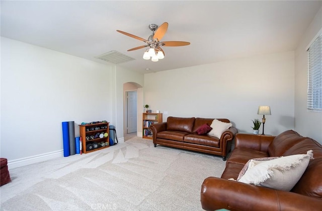 living area featuring arched walkways, a ceiling fan, baseboards, and carpet floors