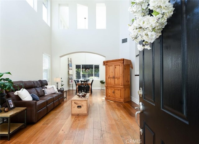 entrance foyer with arched walkways, a high ceiling, light wood-style flooring, and baseboards