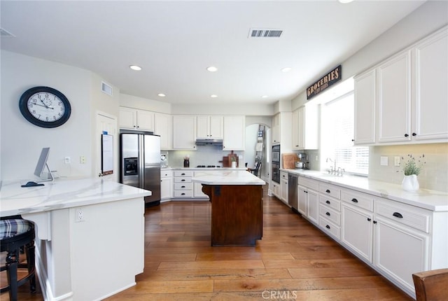 kitchen with stainless steel appliances, white cabinetry, under cabinet range hood, a breakfast bar, and a peninsula