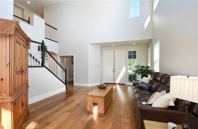 living room with stairway, a towering ceiling, hardwood / wood-style floors, and baseboards