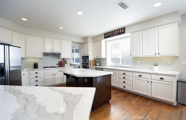 kitchen with refrigerator with ice dispenser, under cabinet range hood, arched walkways, white cabinetry, and a sink