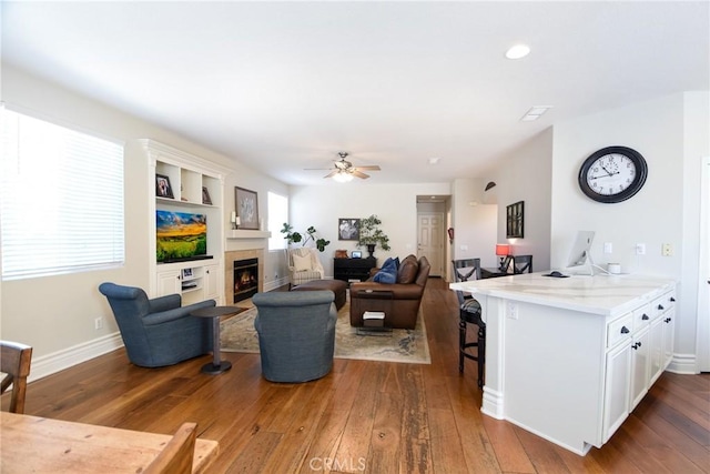 living area with hardwood / wood-style floors, a lit fireplace, a ceiling fan, and baseboards