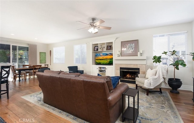 living room with a warm lit fireplace, ceiling fan, wood finished floors, and recessed lighting