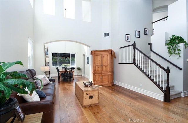 living room with arched walkways, a high ceiling, light wood-style flooring, baseboards, and stairs