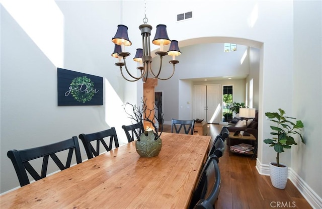 dining room featuring a chandelier, a high ceiling, arched walkways, dark wood finished floors, and baseboards