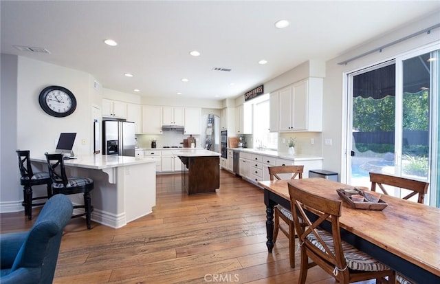 kitchen with stainless steel refrigerator with ice dispenser, hardwood / wood-style floors, white cabinetry, a kitchen island, and recessed lighting