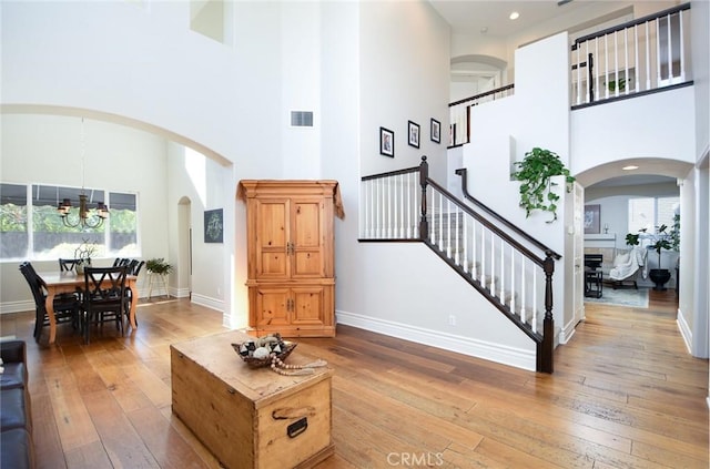 living room with a towering ceiling, a chandelier, light wood-type flooring, arched walkways, and plenty of natural light