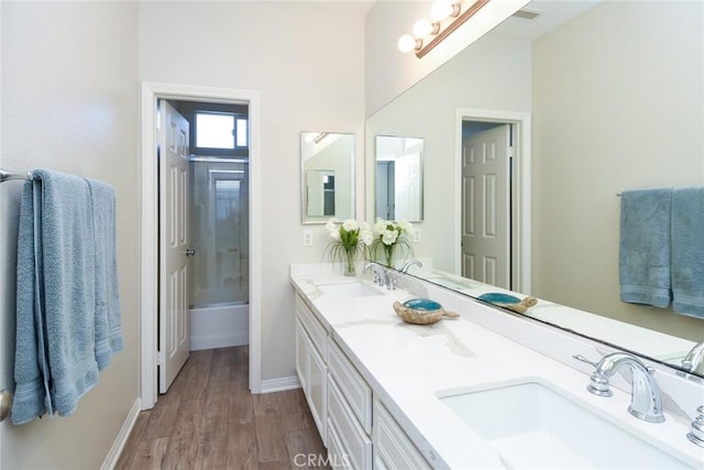 bathroom with wood finished floors, baseboards, double vanity, and  shower combination