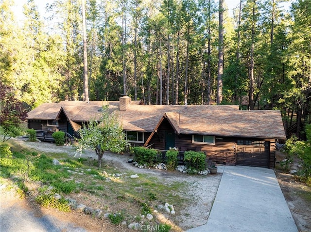 26220 Pine Dell Rd, Idyllwild, CA 92549 - view of front facade featuring an attached garage, concrete driveway, a chimney, and a forest view