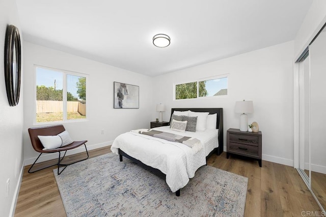 bedroom with multiple windows, wood finished floors, and baseboards