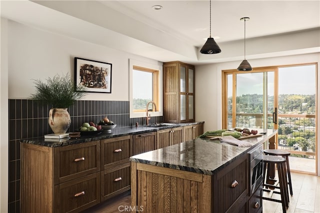 kitchen featuring a sink, wood finished floors, a kitchen island, dark stone countertops, and a kitchen breakfast bar