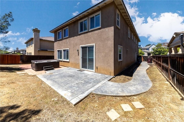 back of property with a hot tub, stucco siding, a fenced backyard, and a patio area
