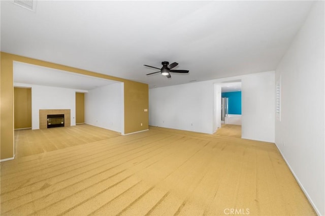 unfurnished living room featuring a ceiling fan, a tiled fireplace, baseboards, and light carpet