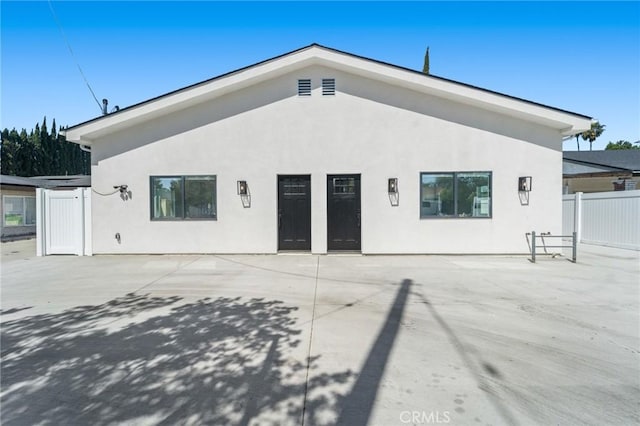 rear view of house with stucco siding, fence, and a patio