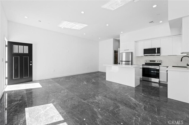 kitchen featuring stainless steel appliances, a sink, dark marble finish floors, a kitchen island, and white cabinets