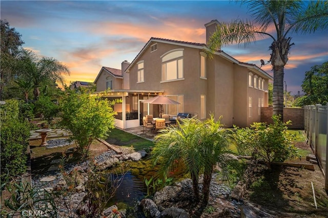 back of property with a chimney, a sunroom, stucco siding, fence, and a patio area