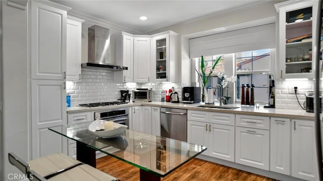 kitchen with appliances with stainless steel finishes, wall chimney exhaust hood, a sink, tasteful backsplash, and recessed lighting