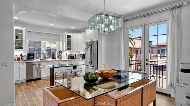 dining area featuring french doors, light wood-type flooring, plenty of natural light, a chandelier, and ornamental molding