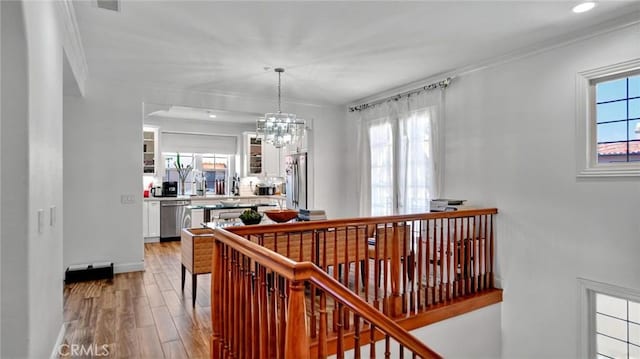 hall with wood finished floors, ornamental molding, a chandelier, recessed lighting, and baseboards