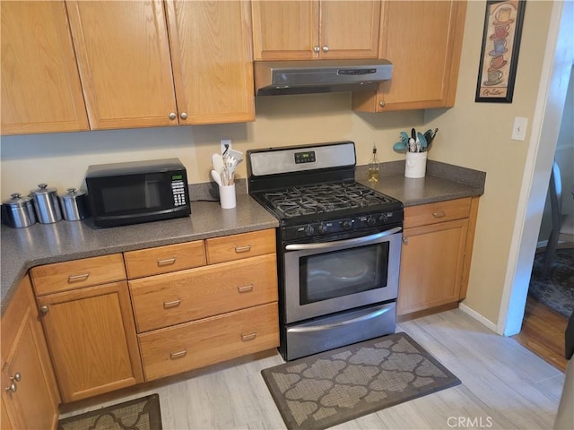kitchen with stainless steel gas range oven, under cabinet range hood, black microwave, and light wood-type flooring