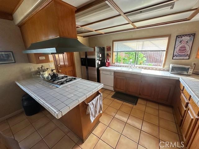 kitchen featuring tile counters, appliances with stainless steel finishes, a sink, exhaust hood, and light tile patterned flooring