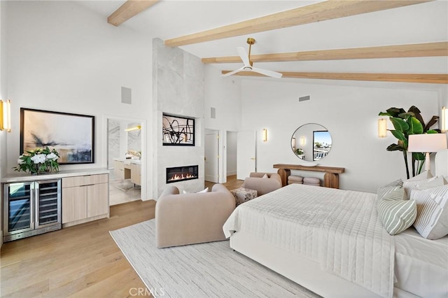 bedroom with wine cooler, beam ceiling, high vaulted ceiling, light wood-type flooring, and a fireplace
