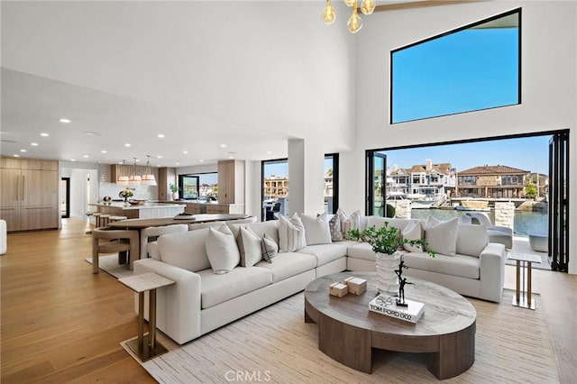 living room with recessed lighting, light wood-style floors, a chandelier, and a high ceiling