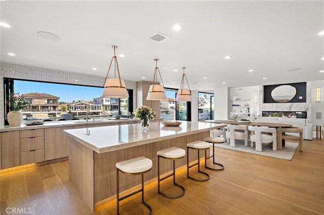 kitchen with modern cabinets, light wood finished floors, a large island, light brown cabinetry, and a breakfast bar area