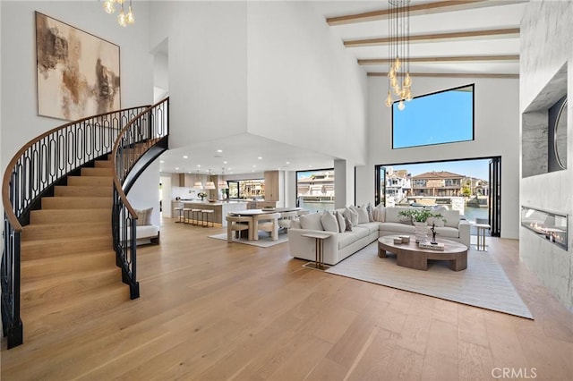 living area with a high ceiling, a chandelier, wood finished floors, stairs, and beamed ceiling