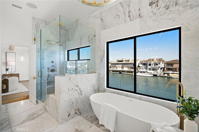 full bathroom with a marble finish shower, marble tiled flooring, a freestanding bath, a water view, and tile walls