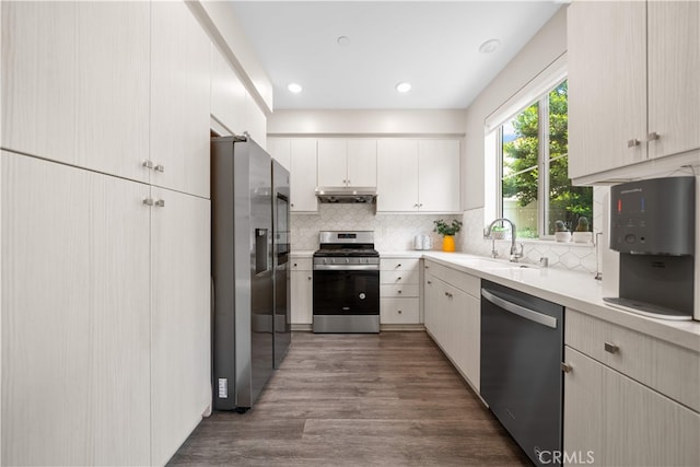 kitchen with stainless steel appliances, a sink, light countertops, under cabinet range hood, and dark wood-style floors
