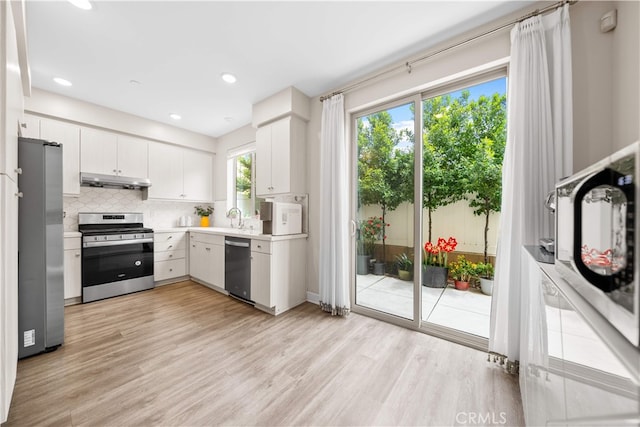 kitchen featuring appliances with stainless steel finishes, a sink, light countertops, light wood-type flooring, and backsplash