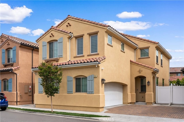 mediterranean / spanish-style home featuring a garage, decorative driveway, a tile roof, fence, and stucco siding