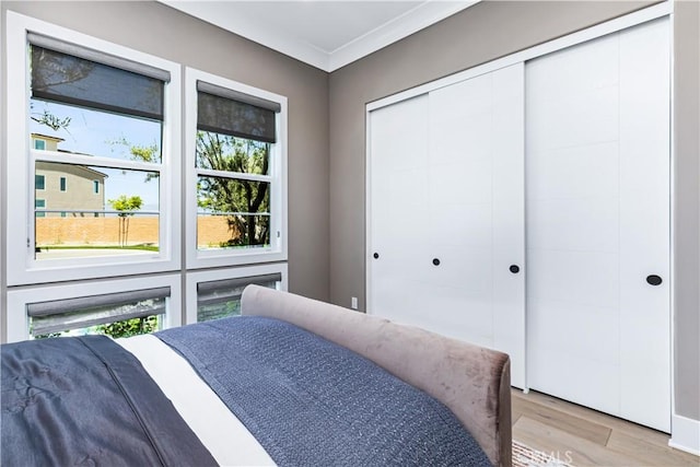 bedroom featuring light wood-style floors, multiple windows, ornamental molding, and a closet