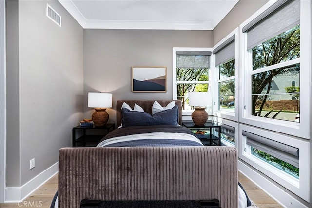bedroom with ornamental molding, multiple windows, light wood finished floors, and baseboards