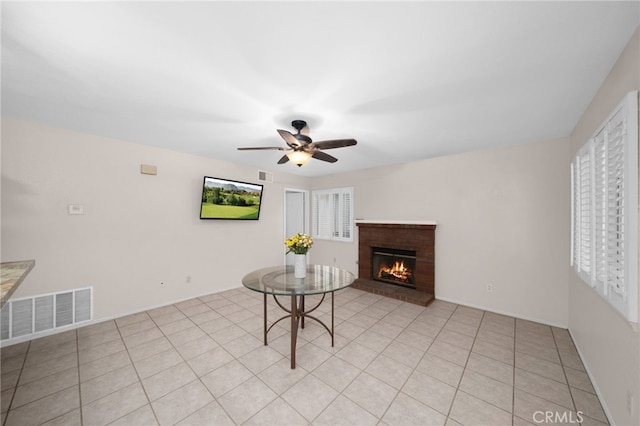 living area with ceiling fan, a brick fireplace, and light tile patterned floors
