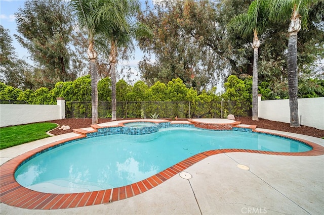 view of swimming pool with fence, a pool with connected hot tub, view of wooded area, and a patio area