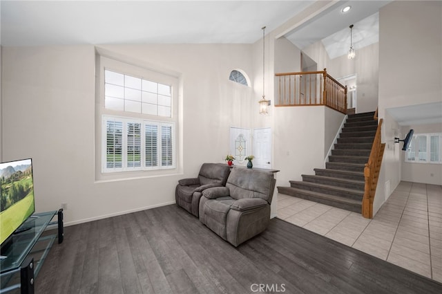 sitting room with wood finished floors, stairs, high vaulted ceiling, healthy amount of natural light, and baseboards