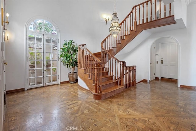 foyer entrance featuring baseboards, stairs, arched walkways, a high ceiling, and a chandelier