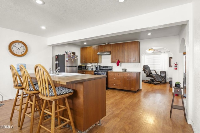 320 D St, Fillmore, CA 93015 - kitchen featuring stainless steel appliances, a kitchen breakfast bar, wood finished floors, arched walkways, and brown cabinetry
