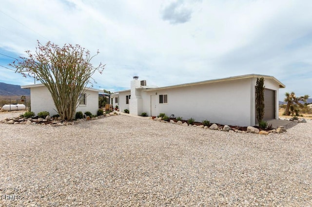 rear view of house featuring a chimney, an attached garage, stucco siding, and gravel driveway