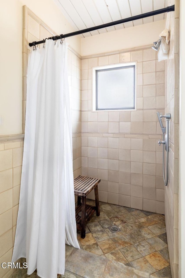 full bathroom featuring tile walls, a tile shower, and stone finish floors