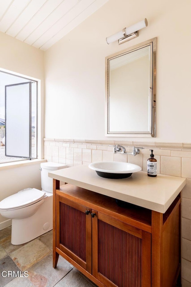 bathroom featuring tile walls, toilet, vanity, and a wainscoted wall