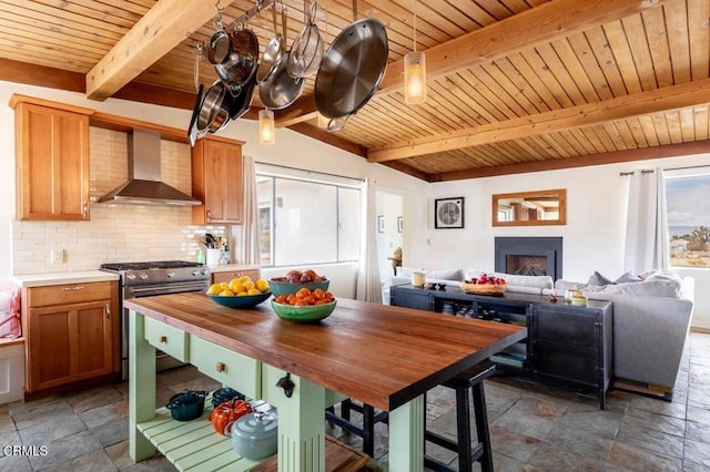 kitchen featuring stainless steel gas range, wall chimney range hood, stone tile flooring, wooden ceiling, and beam ceiling